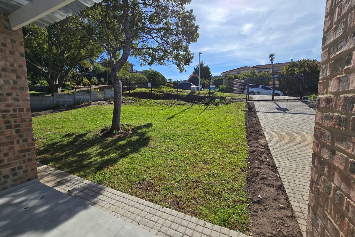 A well-maintained rear garden featuring a paved driveway, lawn area, and secure boundary walling, providing a private outdoor space.