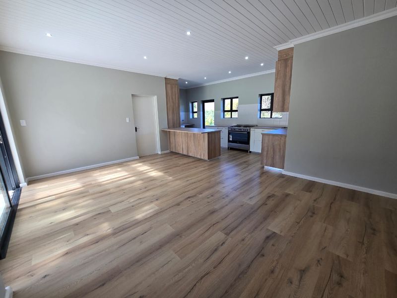 Spacious open-plan living area featuring modern laminate flooring, a tongue and groove ceiling with recessed lighting, and a contemporary kitchen with a central island.