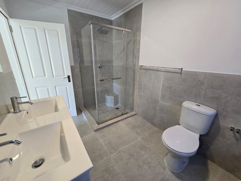 A modern bathroom featuring a double vanity, a glass-enclosed shower with a built-in seat, and grey floor-to-ceiling tiling.