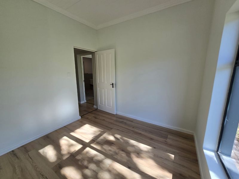 A bright, empty bedroom featuring modern laminate flooring, neutral walls, and coving, with a view into an adjacent room.