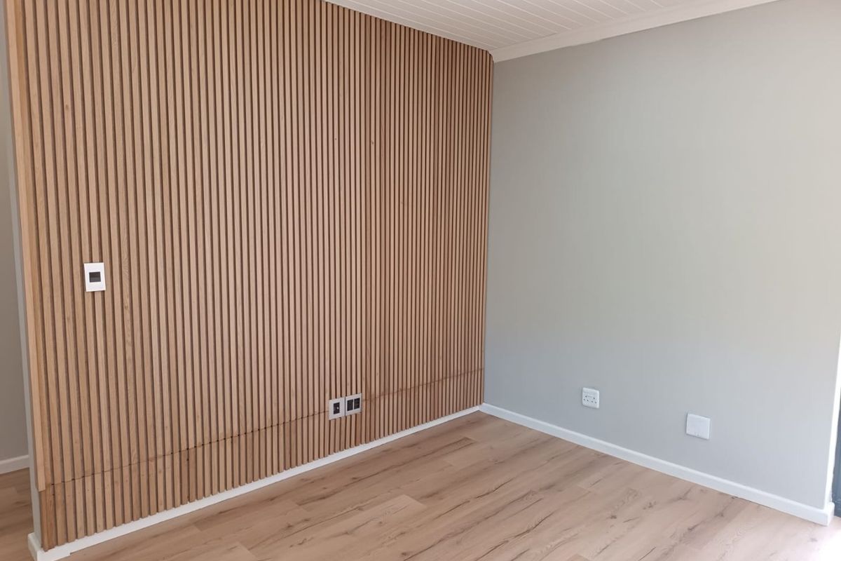 A modern, empty bedroom featuring a stylish timber slat feature wall, light laminate flooring, and a clean tongue and groove ceiling finish.