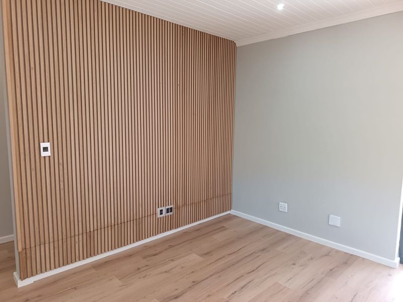 A modern, empty bedroom featuring a stylish timber slat feature wall, light laminate flooring, and a clean tongue and groove ceiling finish.