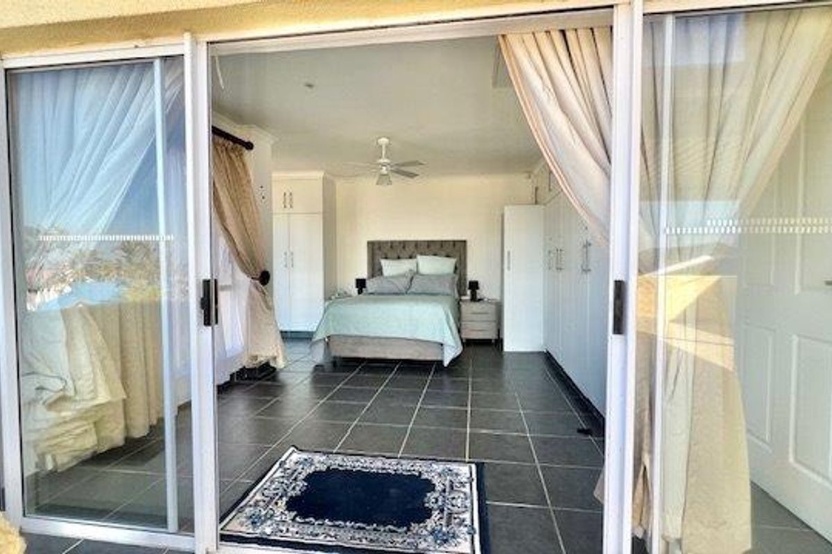 Spacious bedroom featuring tiled flooring, built-in cupboards, a ceiling fan, and large sliding glass doors providing access to the outdoor area.