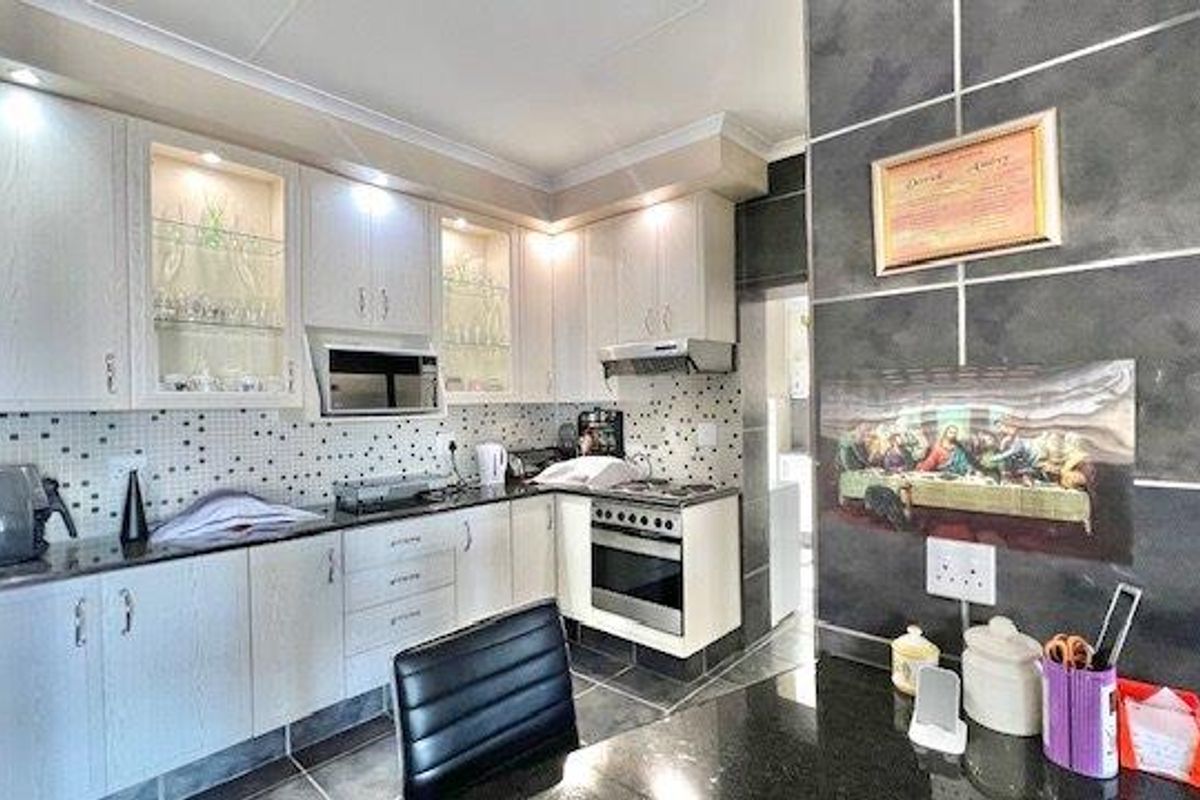 Modern kitchen featuring white cabinetry, granite countertops, mosaic tile backsplash, and integrated appliances including an oven, extractor fan, and built-in microwave.