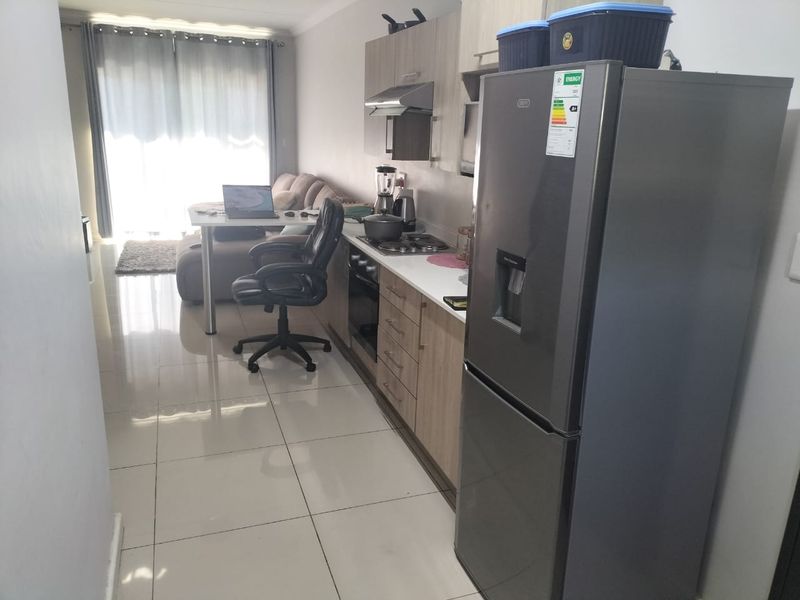 Open-plan living area featuring a modern kitchen with built-in cabinetry, hob, oven, and extractor fan, leading to a bright living space with tiled flooring.