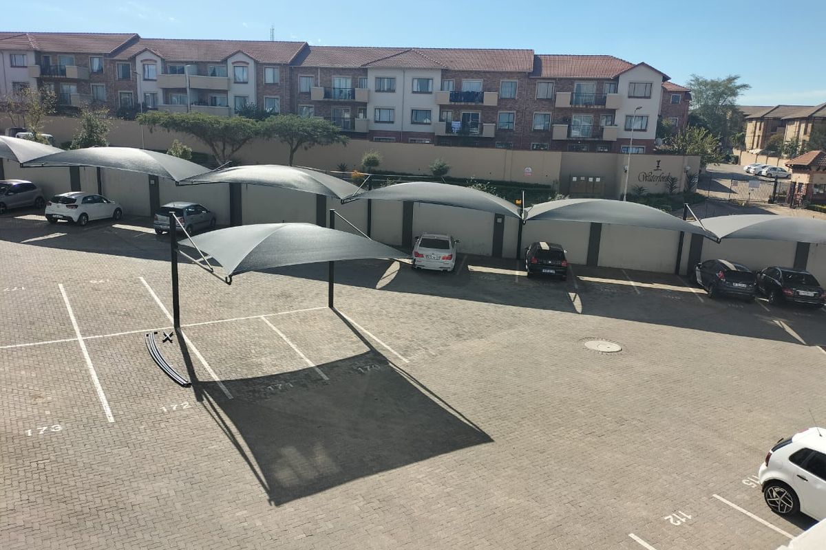 An elevated view of a paved residential parking area featuring multiple shade cloth carports and a secure perimeter wall.