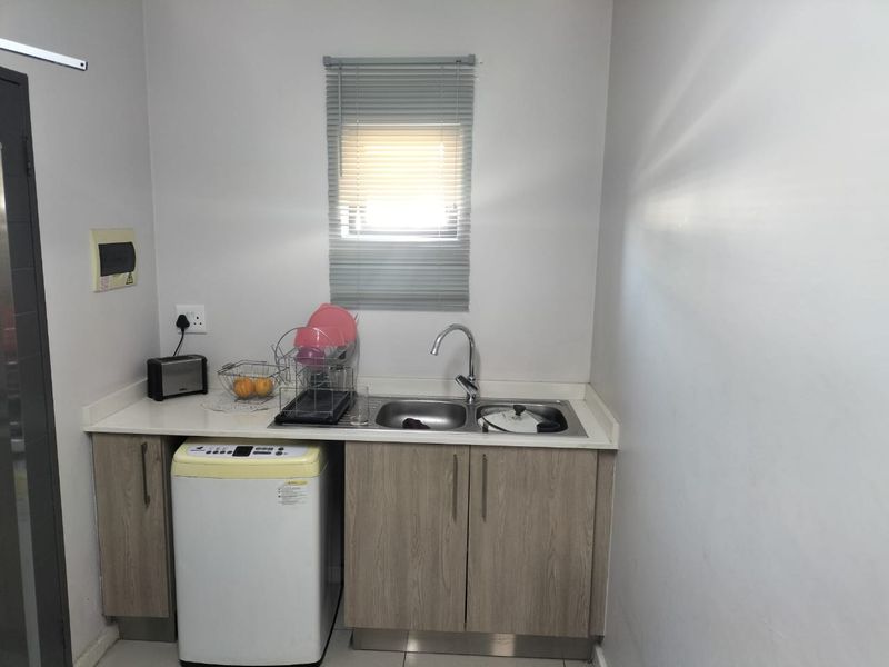 A functional laundry area featuring laminate cabinetry, a stainless steel double sink with mixer tap, and a window with a venetian blind.