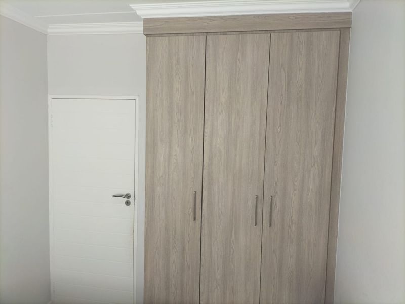 A clean bedroom interior featuring a modern wood-finish built-in wardrobe and classic crown molding detail.