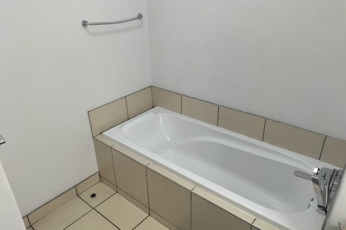A clean, functional bathroom featuring a built-in bathtub with neutral tiled surround and floor, complemented by chrome fixtures.