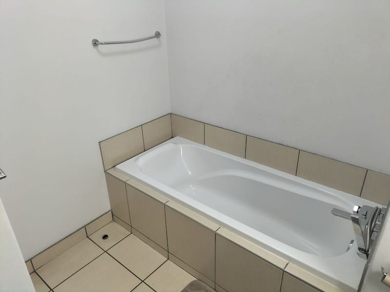 A clean, functional bathroom featuring a built-in bathtub with neutral tiled surround and floor, complemented by chrome fixtures.