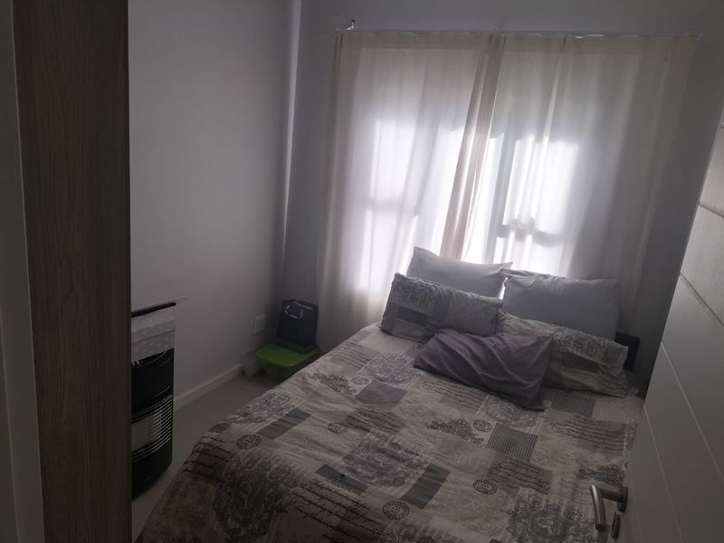A compact bedroom featuring neutral wall finishes and a window with sheer curtains, providing natural light.