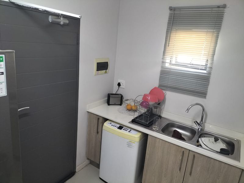 Compact laundry area featuring built-in cabinetry, a stainless steel sink with mixer tap, and a window with fitted venetian blinds.