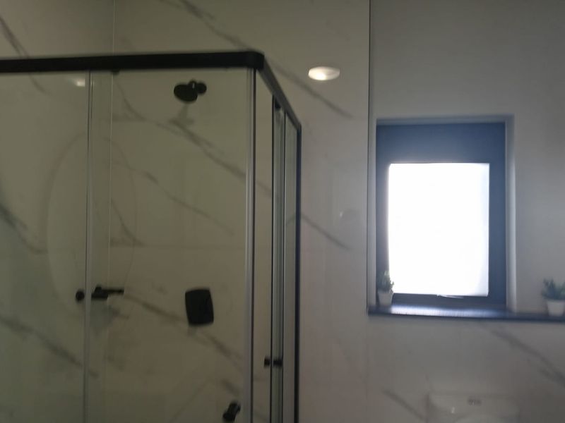 Modern bathroom featuring a glass shower enclosure with black fixtures and elegant marble-look wall tiling.