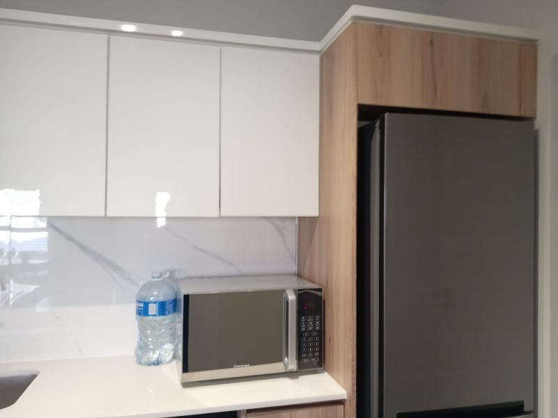 Modern kitchen featuring white gloss and wood-look cabinetry, marble-effect splashback, and stone countertops with integrated fridge housing.