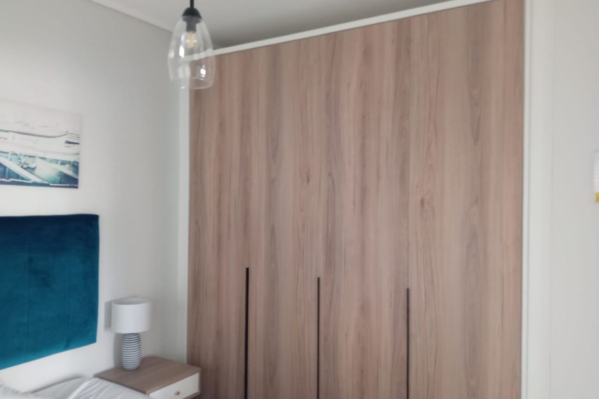 A bedroom featuring modern wood-finish built-in wardrobes and a contemporary pendant light fixture.