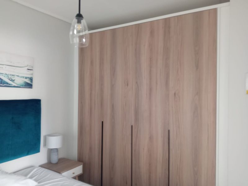 A bedroom featuring modern wood-finish built-in wardrobes and a contemporary pendant light fixture.