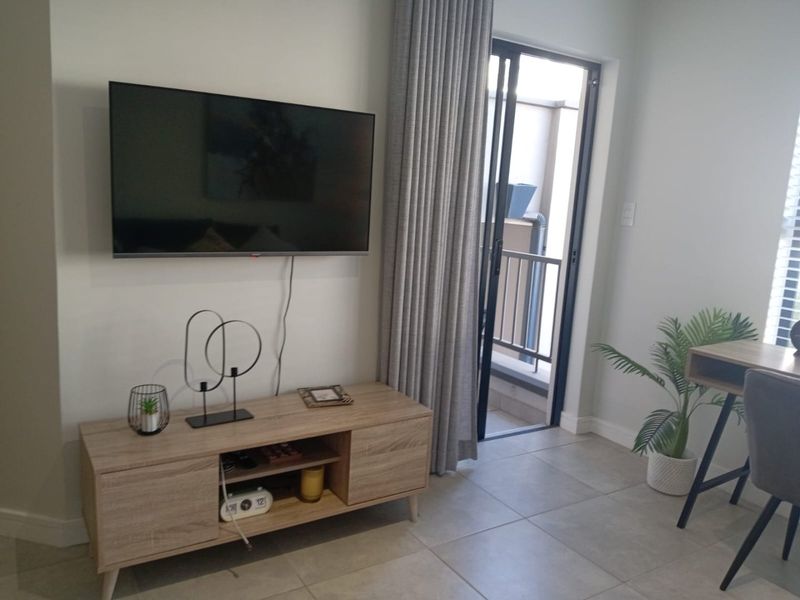 A modern living area featuring tiled flooring, a wall-mounted television, and direct access to a private balcony through a sliding glass door.