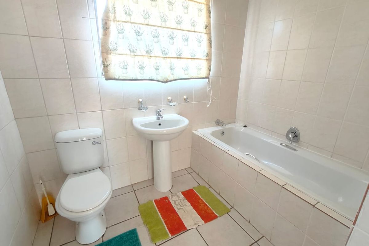 A functional bathroom featuring a pedestal washbasin, built-in bathtub, and neutral ceramic tiling throughout.