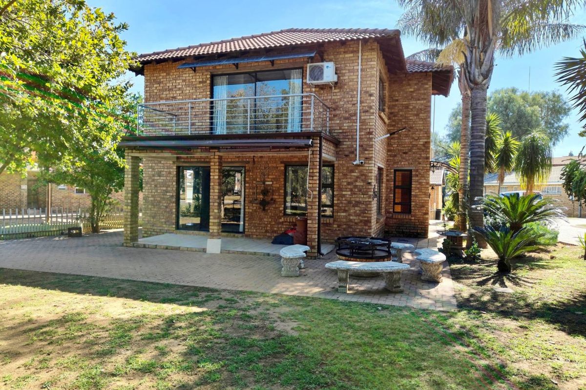Rear view of a double-story face brick house featuring a paved patio area, a balcony with stainless steel balustrades, and established garden surroundings.
