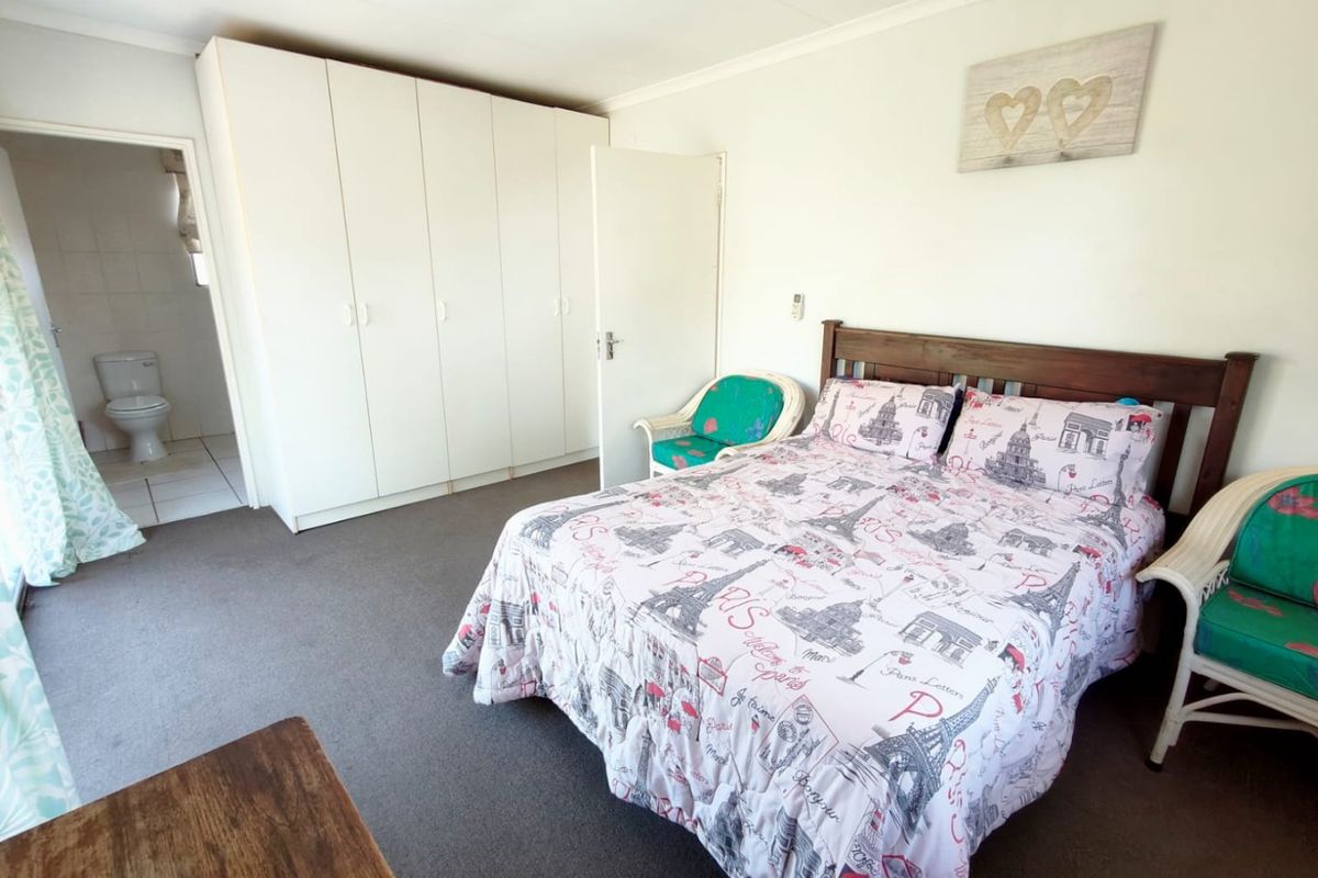 A spacious bedroom featuring built-in cupboards and an attached en-suite bathroom with neutral finishes.