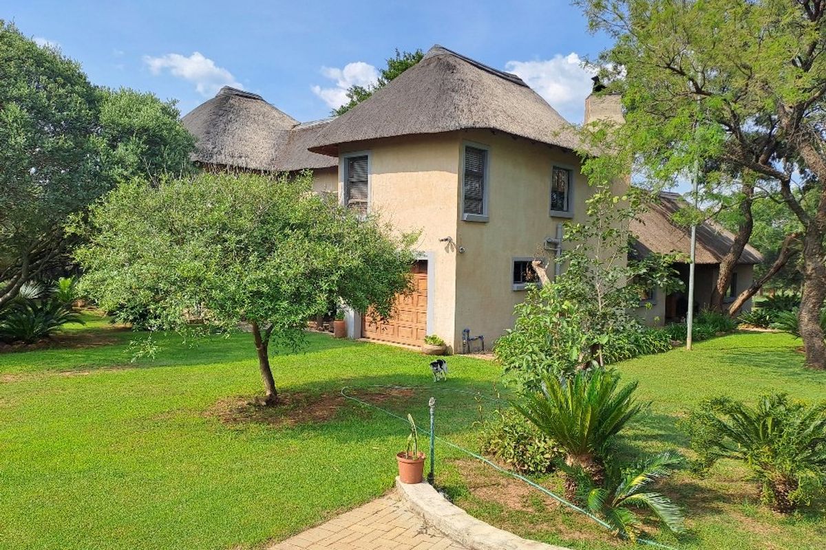 A view of the rear exterior of a two-story farmhouse featuring a traditional thatched roof, stucco facade, and a well-maintained garden.