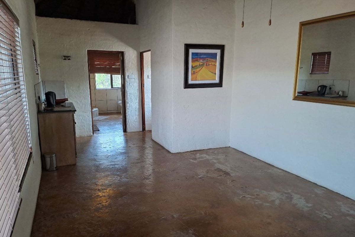 A rustic living area featuring exposed thatch ceiling, textured walls, and polished concrete flooring, with direct access to an adjoining bathroom.