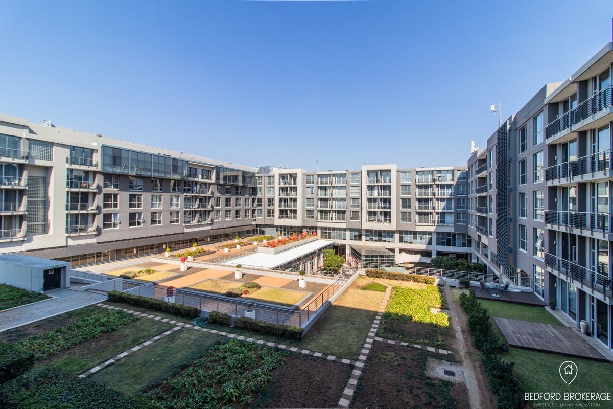 An elevated view of the apartment complex courtyard featuring landscaped garden areas, paved pathways, and private balconies overlooking the central outdoor space.