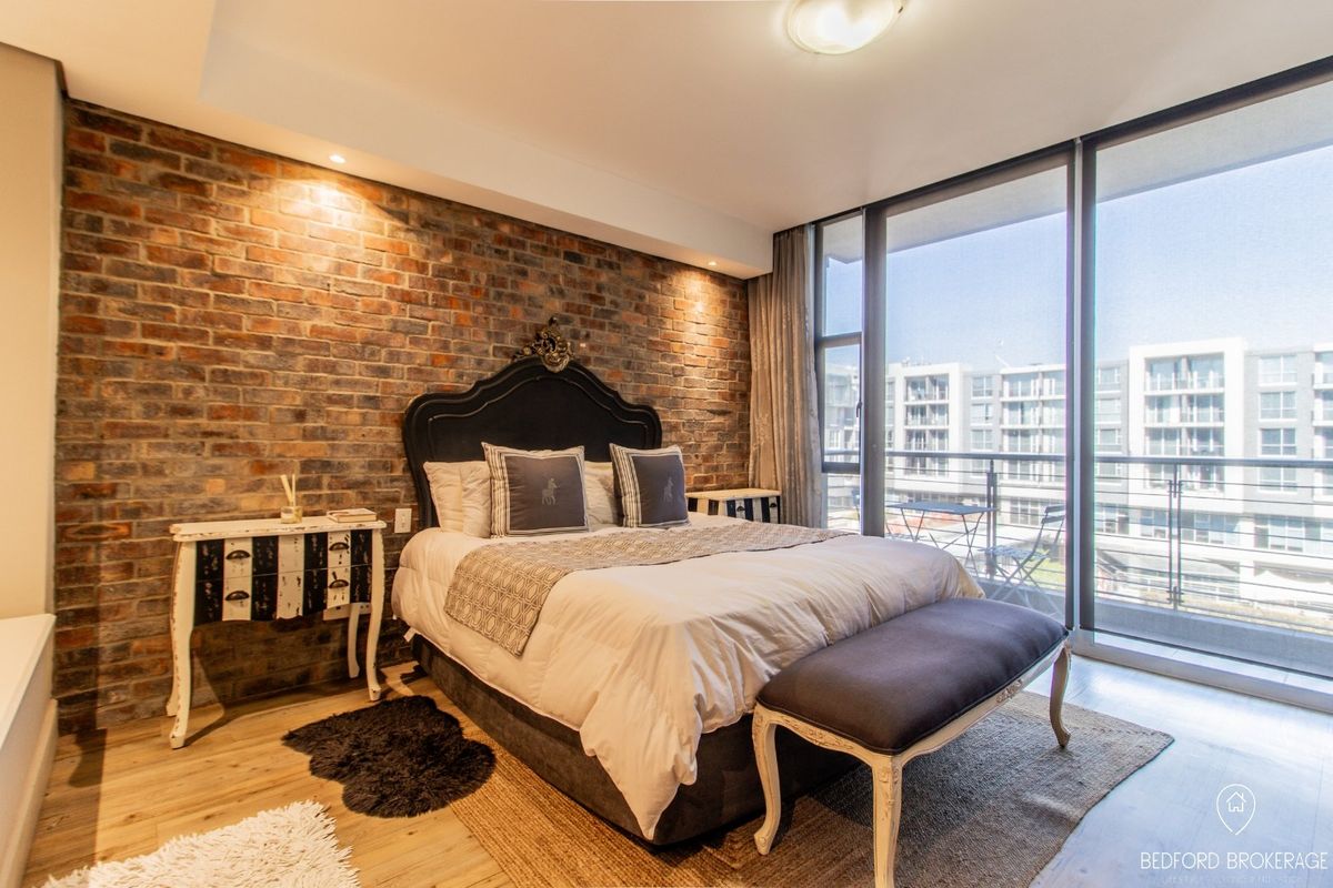 Modern bedroom featuring an exposed brick accent wall, recessed lighting, and large sliding glass doors opening to a private balcony.