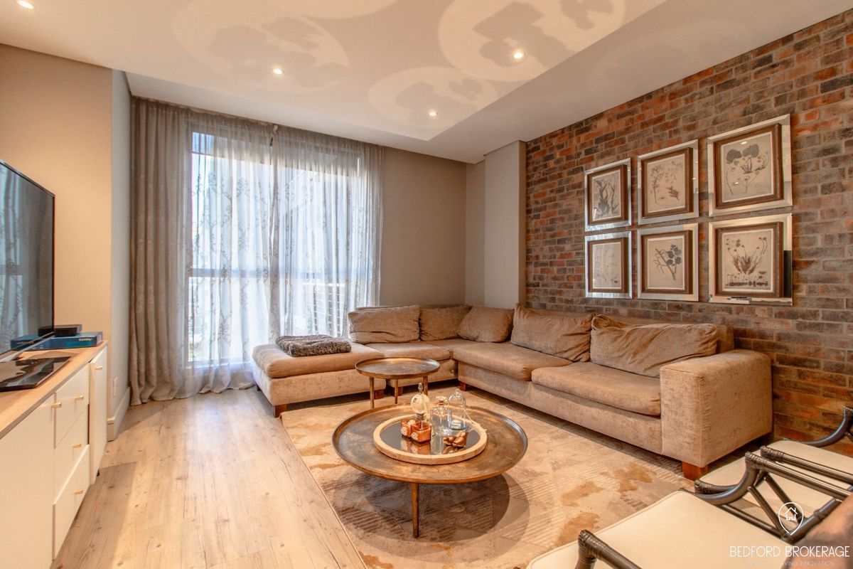 A well-maintained living room featuring an exposed brick accent wall, modern laminate flooring, and recessed ceiling lighting.