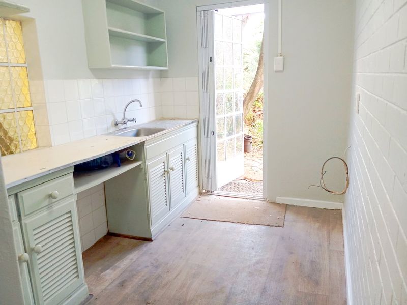 A functional scullery or utility area featuring built-in cabinetry, a stainless steel sink, and direct access to the exterior through a glass-paneled door.