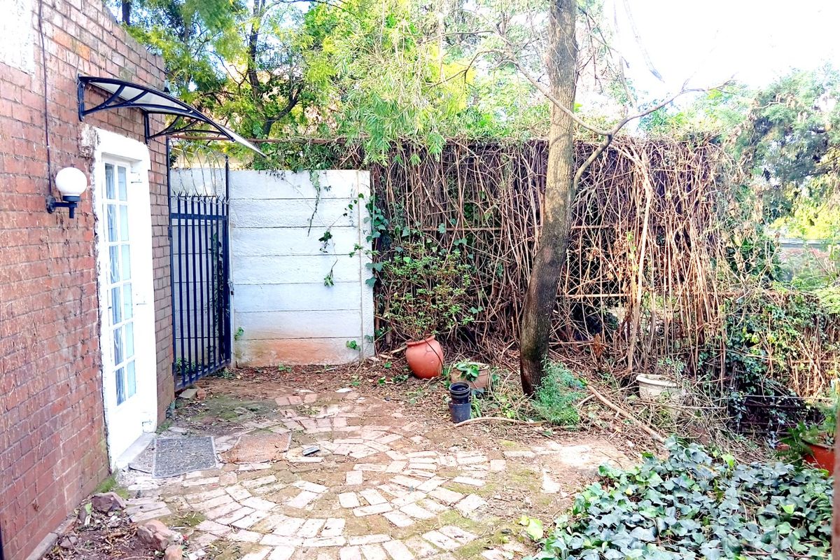 A rear exterior area featuring brick paving, a security gate, and an awning, currently requiring landscaping and maintenance to improve its appeal.