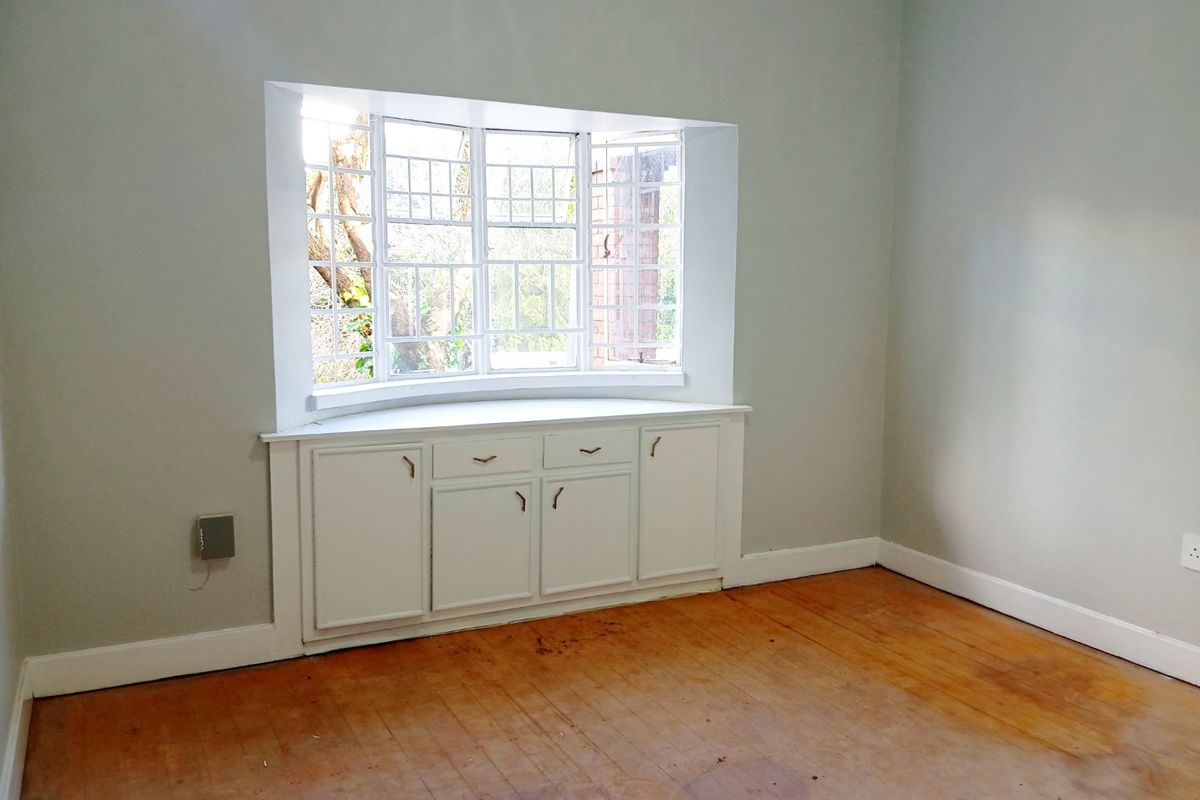 An empty bedroom featuring a classic bay window with integrated storage cabinetry and original hardwood flooring in need of refinishing.