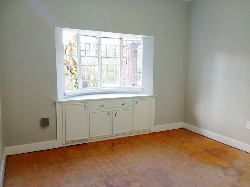 An empty bedroom featuring a classic bay window with integrated storage cabinetry and original hardwood flooring in need of refinishing.