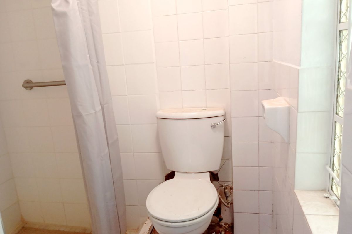 A dated bathroom featuring a toilet and shower area with visible damage to the floor tiles and grout, requiring maintenance or renovation.