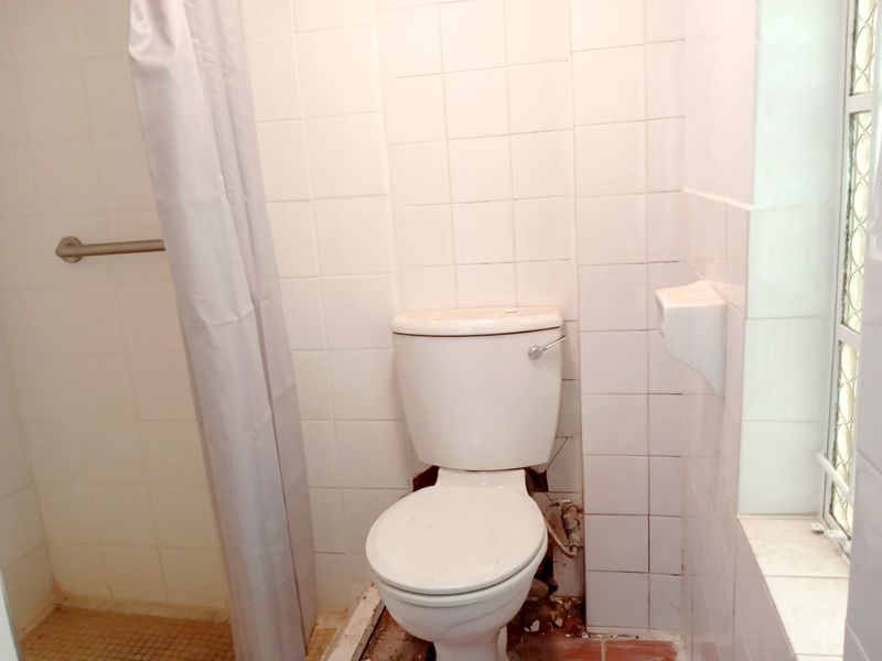 A dated bathroom featuring a toilet and shower area with visible damage to the floor tiles and grout, requiring maintenance or renovation.