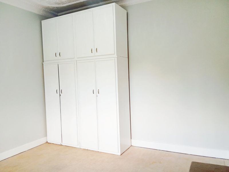 A vacant bedroom featuring white built-in cupboards, ornate ceiling cornicing, and unfinished flooring, offering a blank canvas for potential renovation.