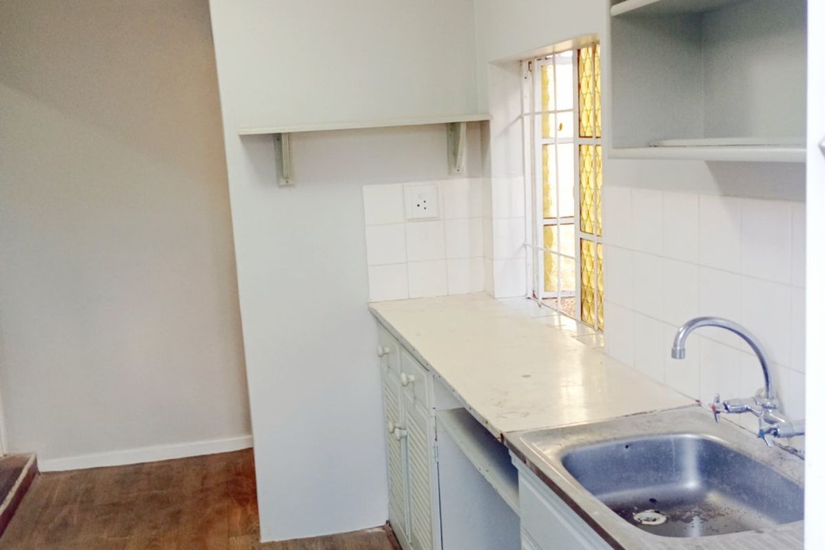 A compact, empty kitchen featuring a stainless steel sink, laminate countertops, and built-in cabinetry with open shelving, ready for renovation or modernization.