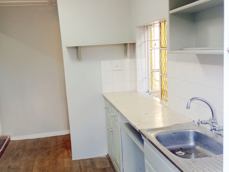 A compact, empty kitchen featuring a stainless steel sink, laminate countertops, and built-in cabinetry with open shelving, ready for renovation or modernization.