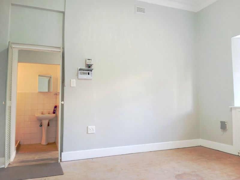 An empty bedroom featuring neutral walls, worn flooring, and an attached small bathroom area with a pedestal basin.