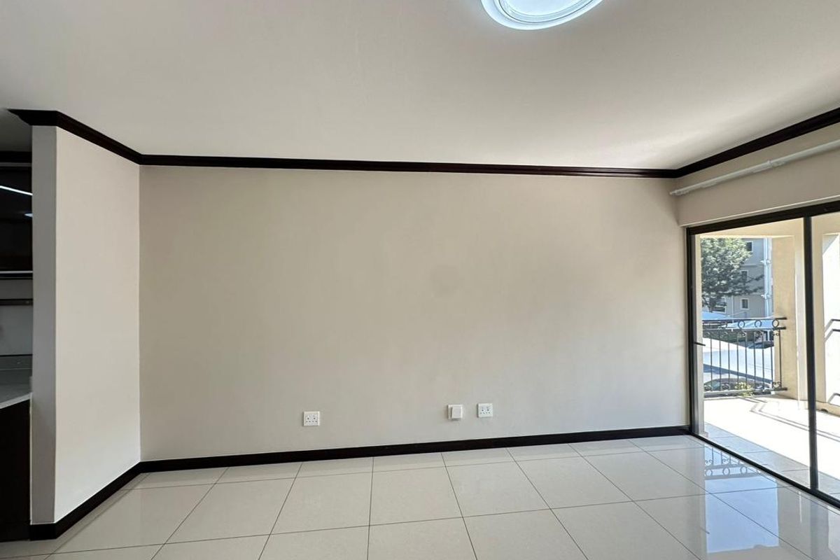 A bright, empty living room featuring neutral tiled flooring, dark trim accents, and a large sliding glass door providing access to an outdoor balcony.