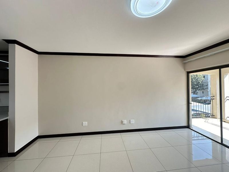 A bright, empty living room featuring neutral tiled flooring, dark trim accents, and a large sliding glass door providing access to an outdoor balcony.