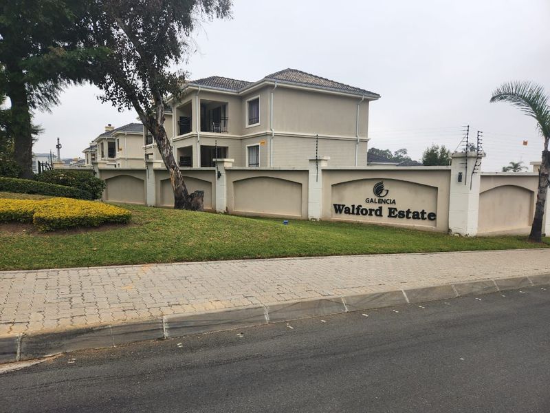 Street view of the Walford Estate entrance, featuring a well-maintained perimeter wall, electric fencing, and multi-story apartment buildings with balconies.