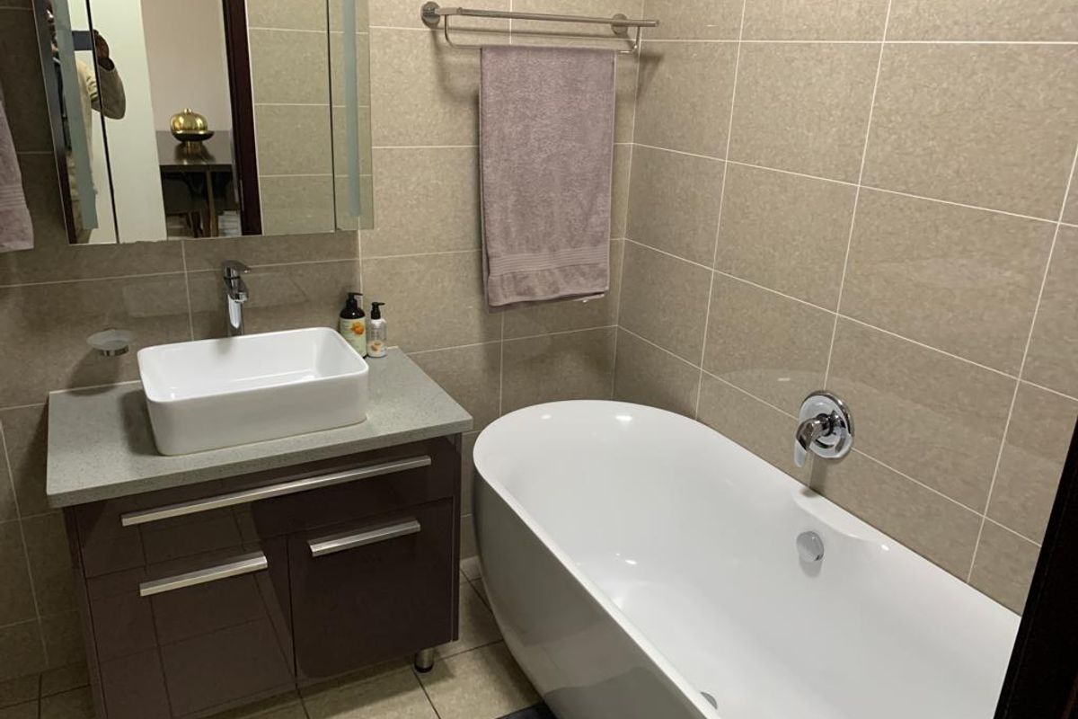 Modern bathroom featuring a sleek freestanding bathtub, a contemporary vessel sink on a vanity cabinet, and neutral wall tiling.