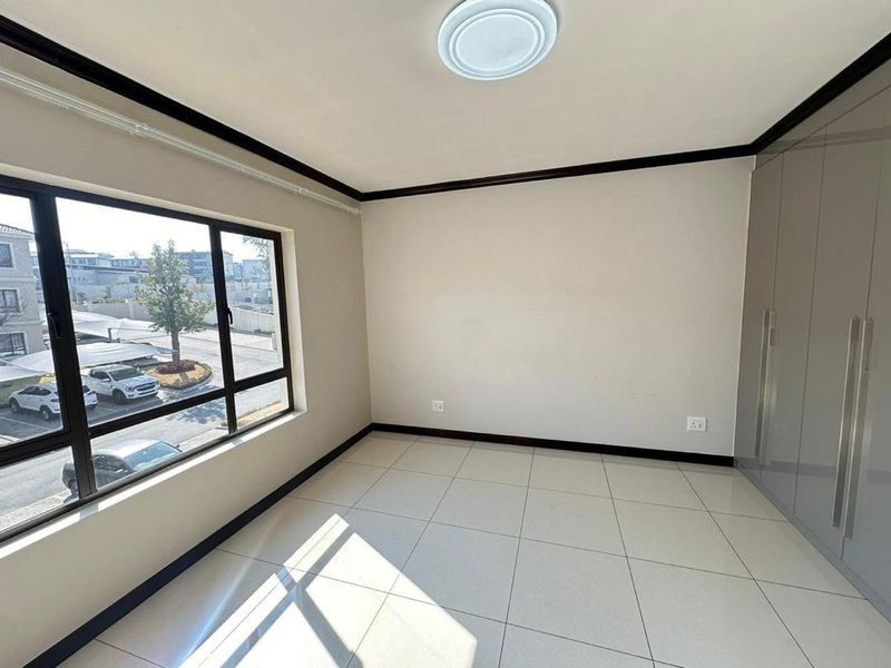 A bright, empty bedroom featuring neutral tiled flooring, built-in cupboards, and large windows providing natural light.