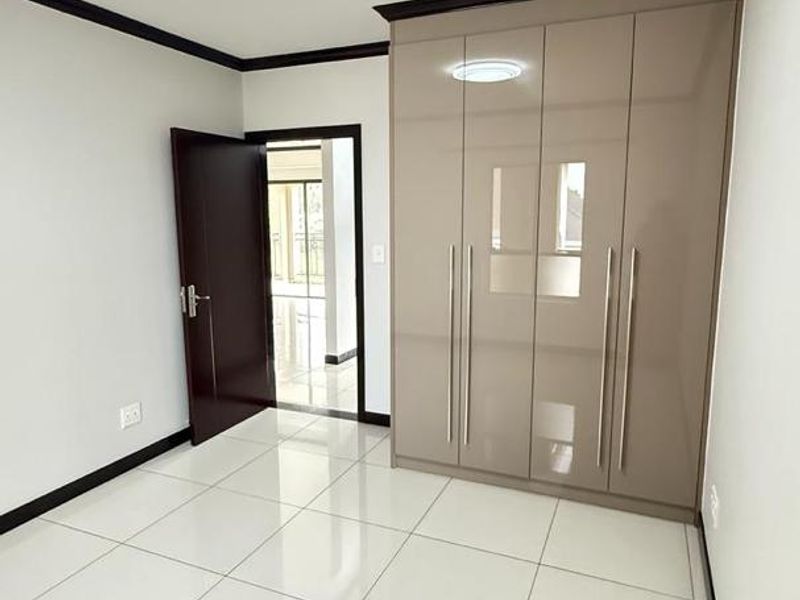 A clean, modern bedroom featuring high-gloss built-in cupboards, neutral tiled flooring, and crisp white walls, offering a bright and versatile living space.