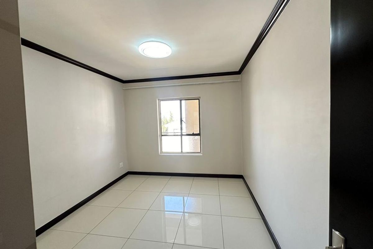 A clean, empty bedroom featuring white walls, dark trim, tiled flooring, and a central ceiling light fixture.
