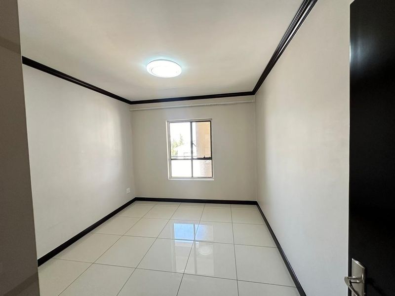 A clean, empty bedroom featuring white walls, dark trim, tiled flooring, and a central ceiling light fixture.