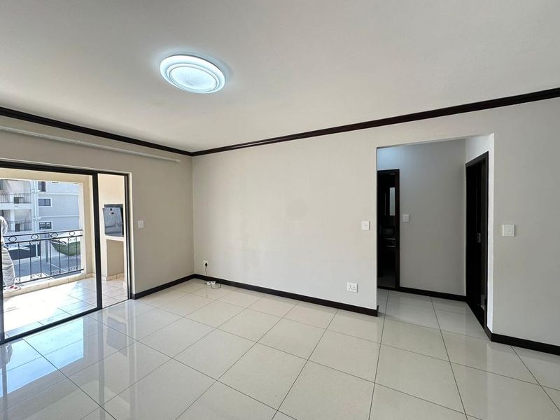 A bright, empty living room featuring neutral tiled flooring, dark trim accents, and direct access to an outdoor balcony area.