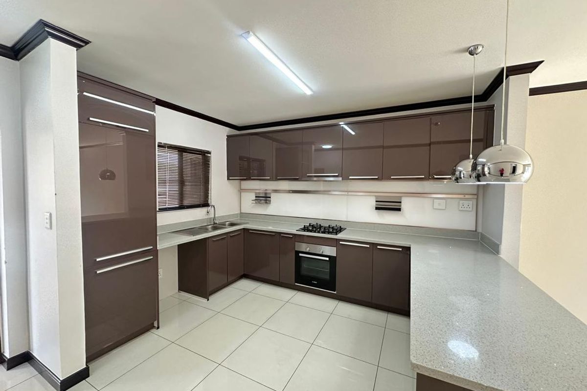 Modern kitchen featuring high-gloss brown cabinetry, stone countertops, built-in oven, gas hob, and tiled flooring in a clean, open-plan layout.