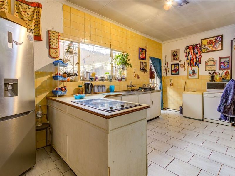 A functional kitchen featuring yellow tiled walls, tiled flooring, built-in cabinetry, and a central hob, offering potential for a modern renovation.